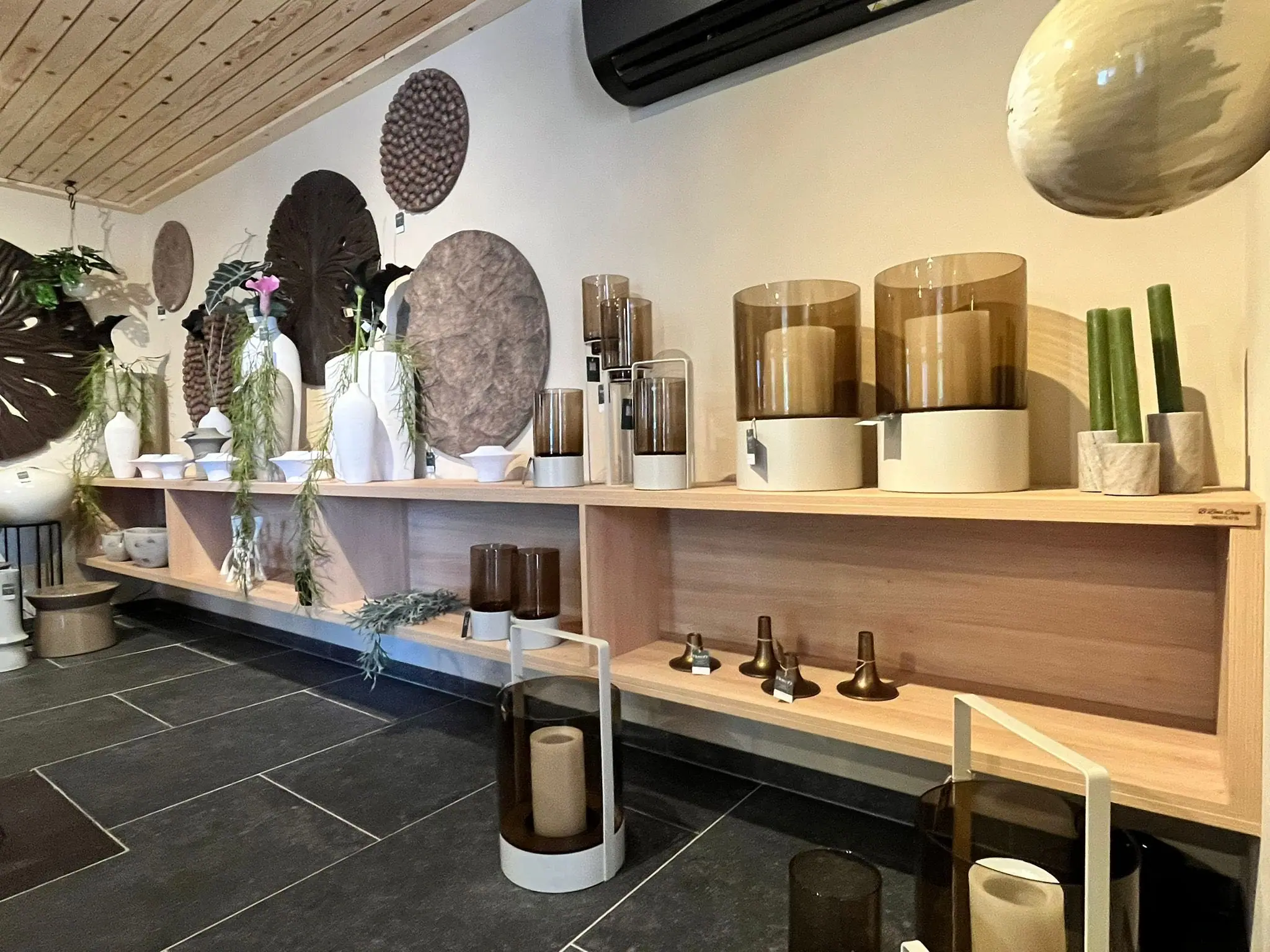 Une longue tablette de chêne massif fixée au mur, objets de présentation posés dessus, sol en pierre sombre