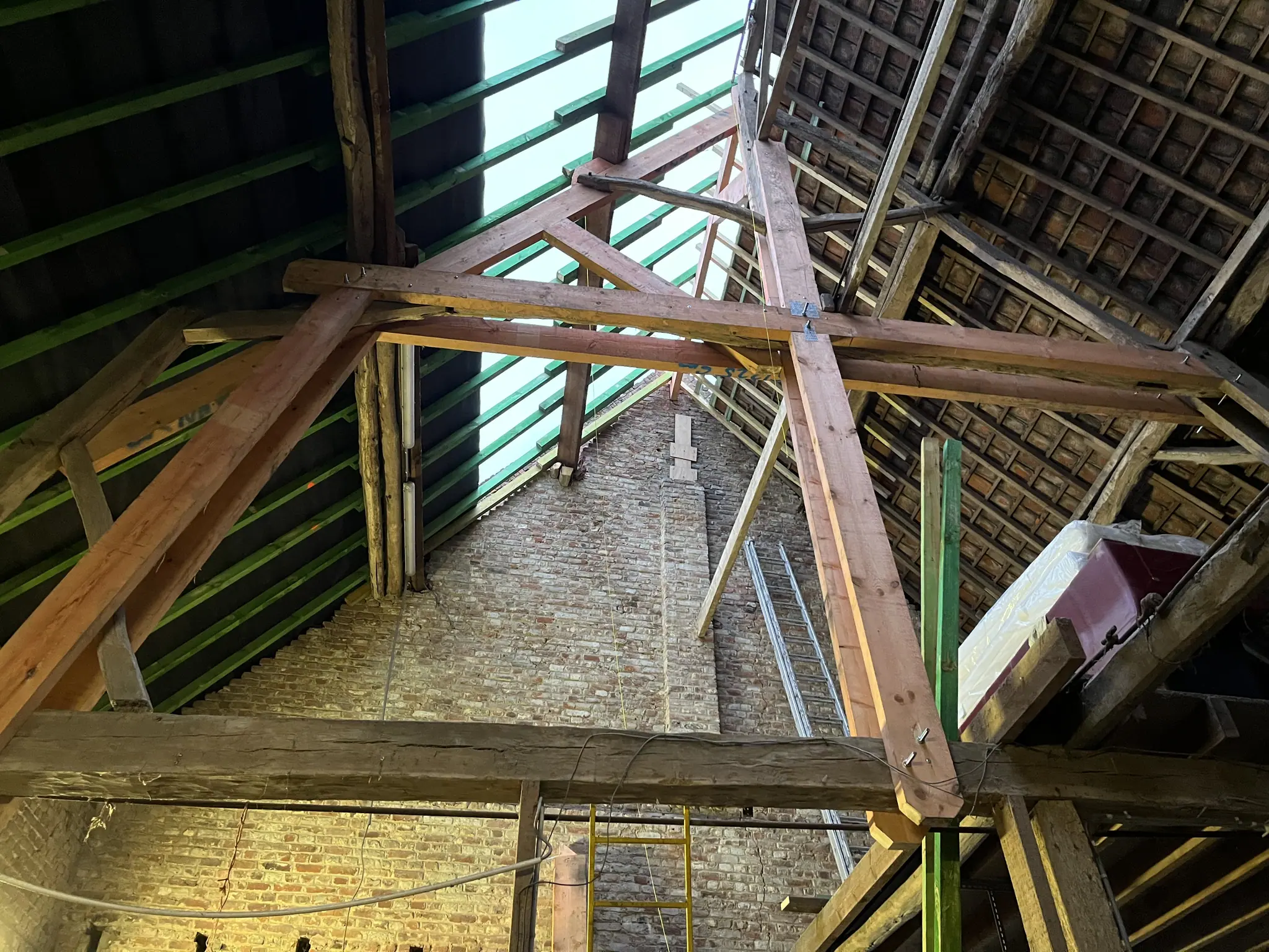 Un assemblage de charpente neuve encastré dans une ferme ancienne noircie, ciel visible entre les chevrons