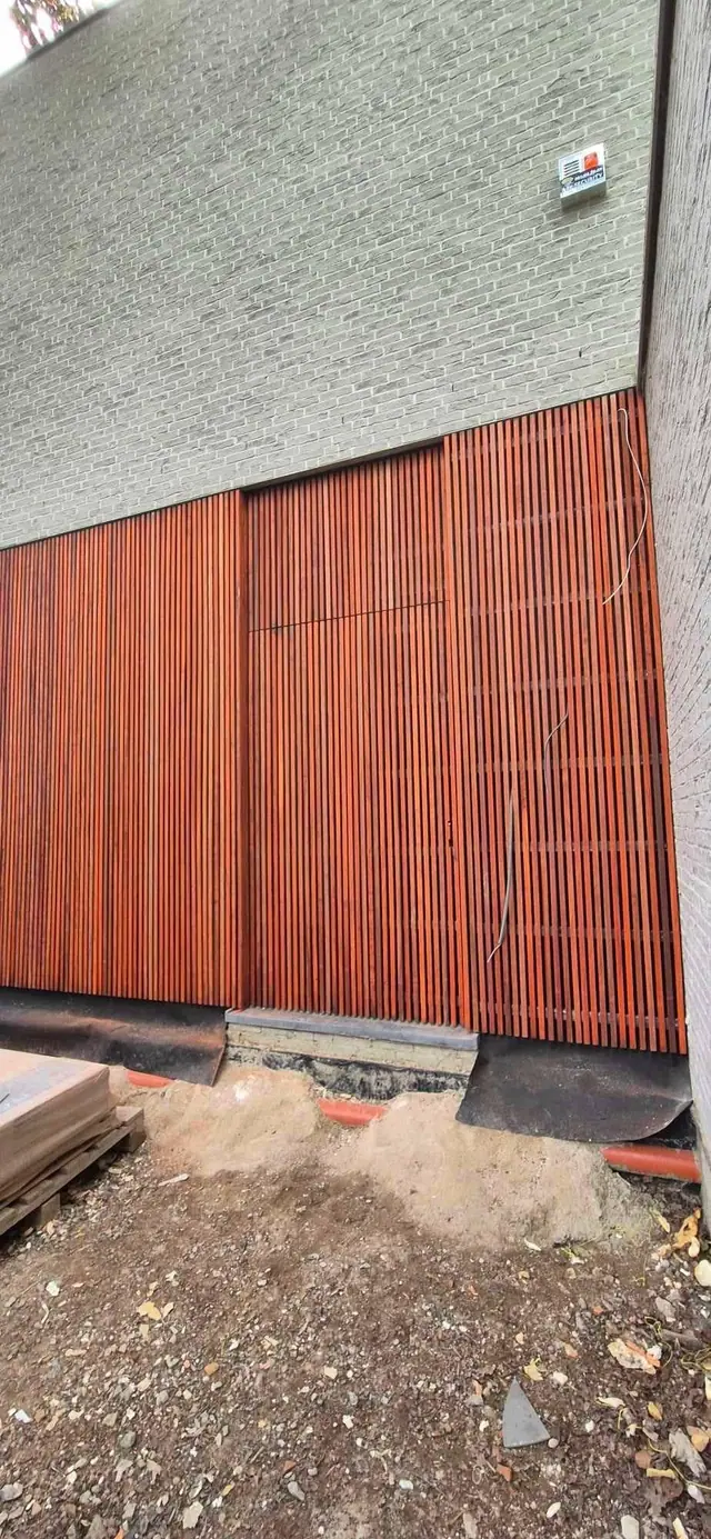 Façade entièrement habillée de tasseaux de padouk verticaux, l’écart entre les lames laissant voir le mur sombre