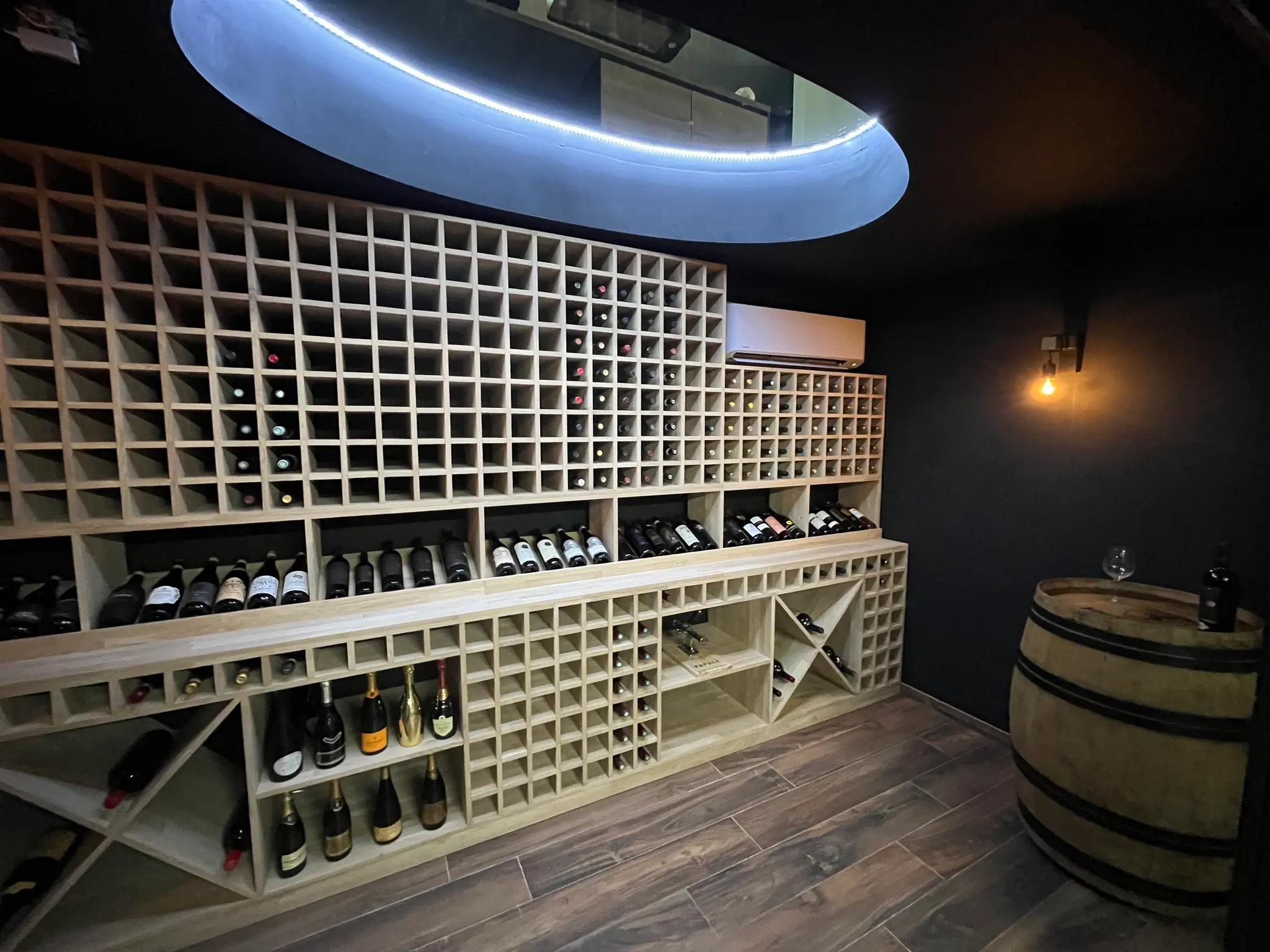 Cave à vin garnie : casier en chêne massif, hublot circulaire et applique chaude sur murs sombres