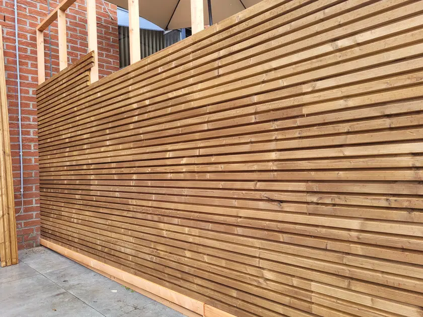 La claire-voie vue en enfilade : les lames horizontales filent entre deux murs de brique, l’ombre les souligne une à une