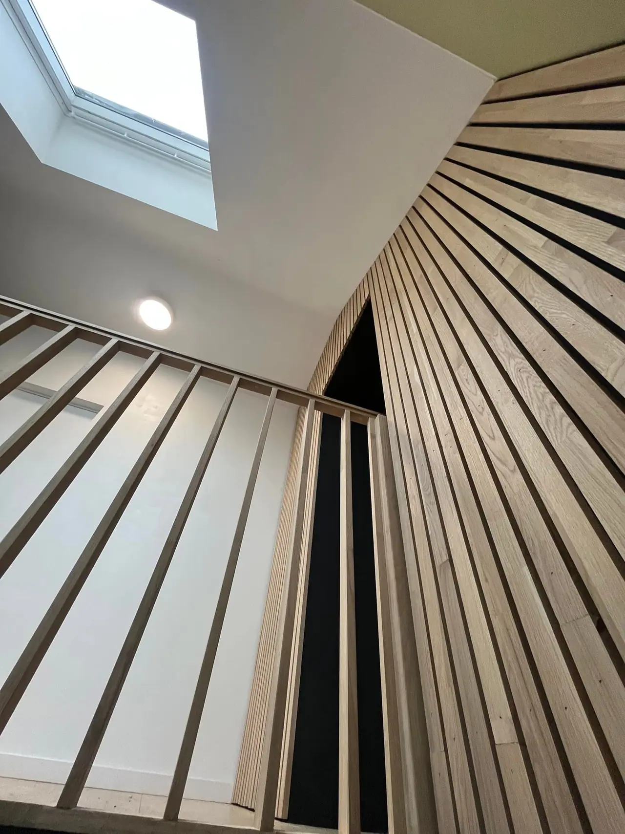 Claustra en lames de chêne verticales déployé en éventail autour d’un escalier