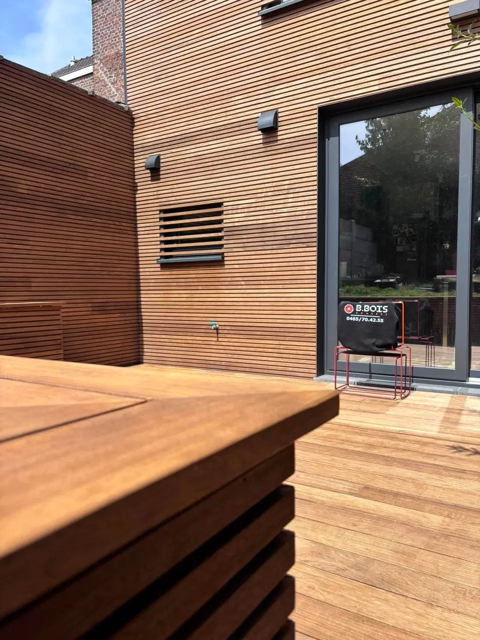Le bord de la terrasse et sa banquette, le bardage et un panneau persienné juste au-dessus