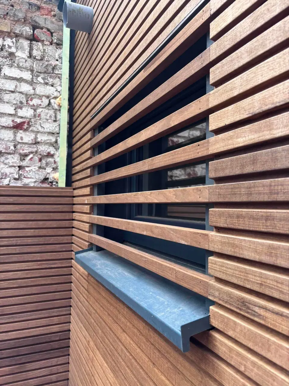Le même panneau contre le mur de brique ancienne, l’appui d’aluminium tranchant sous les lames