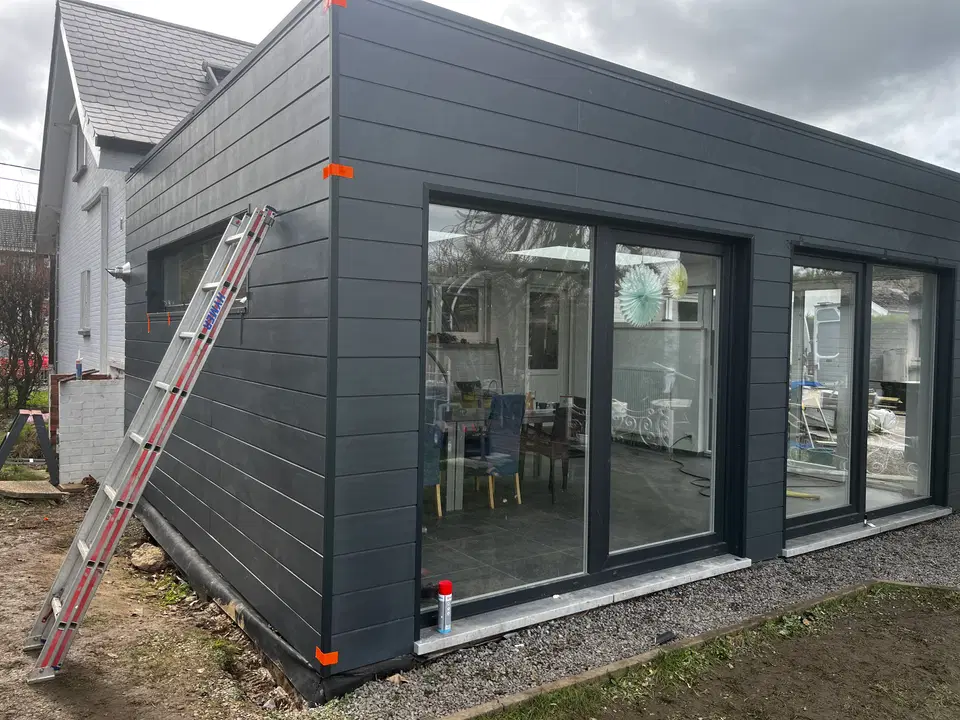 L’extension terminée vue du jardin : bardage anthracite, grandes baies à cadre sombre et angle vitré
