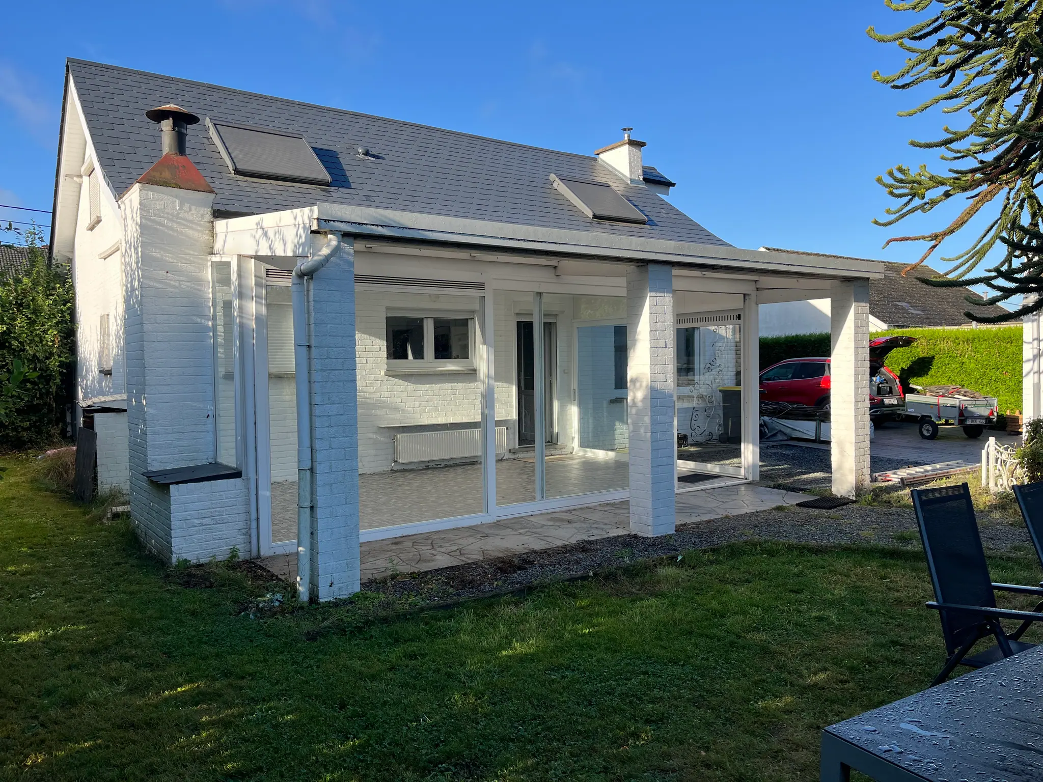 Maison blanche avec une ancienne véranda basse et un auvent, pelouse devant