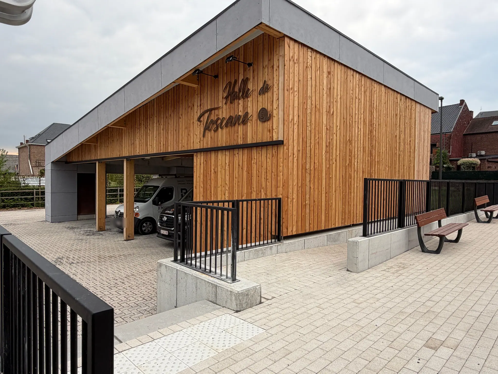 Le pignon de la halle communale de Silly : bardage de bois vertical portant l’enseigne gravée, garde-corps noir et parvis pavé