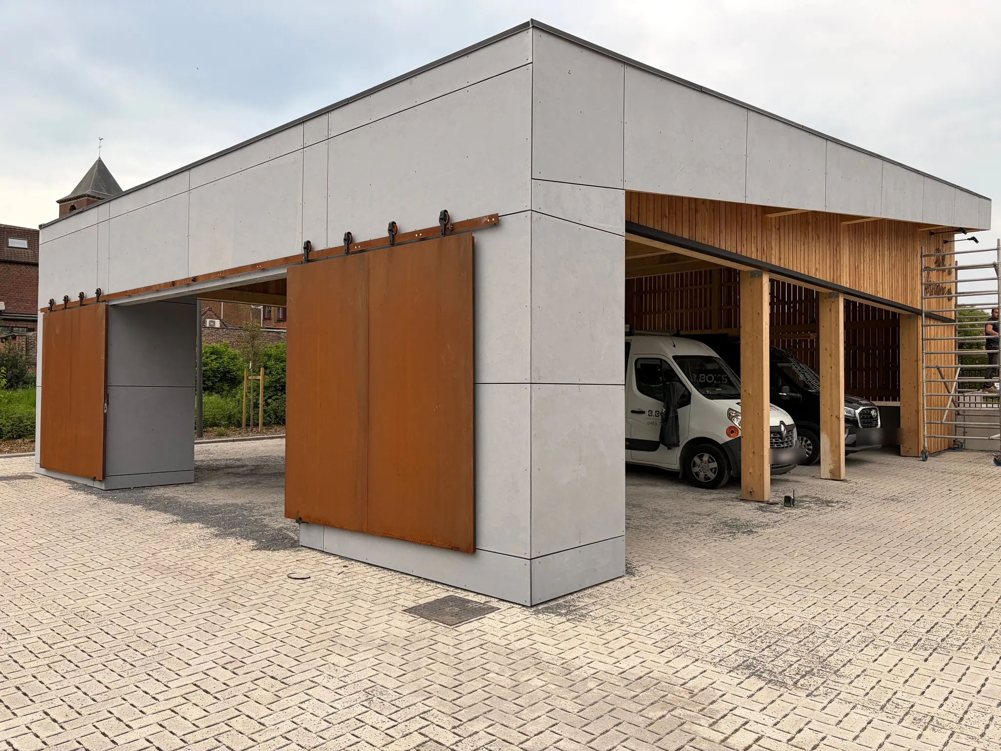 La halle de Silly achevée, vue de trois quarts : panneaux de béton, portes coulissantes en acier corten et parois de bois à claire-voie