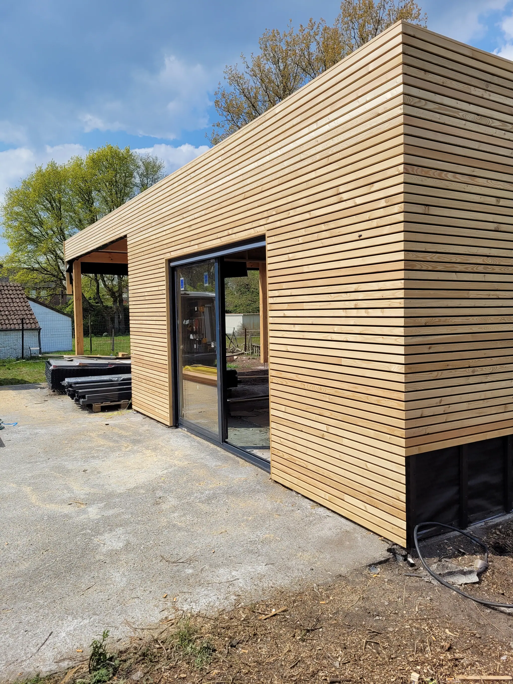 L’angle du pavillon, le carport derrière, et le soubassement noir sous le bardage