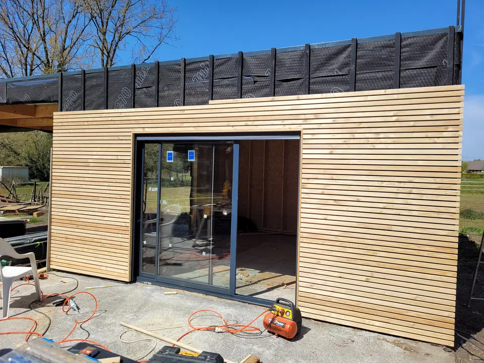 Le volume bardé pendant le chantier : la baie est posée, le compresseur et les tuyaux sont encore au sol