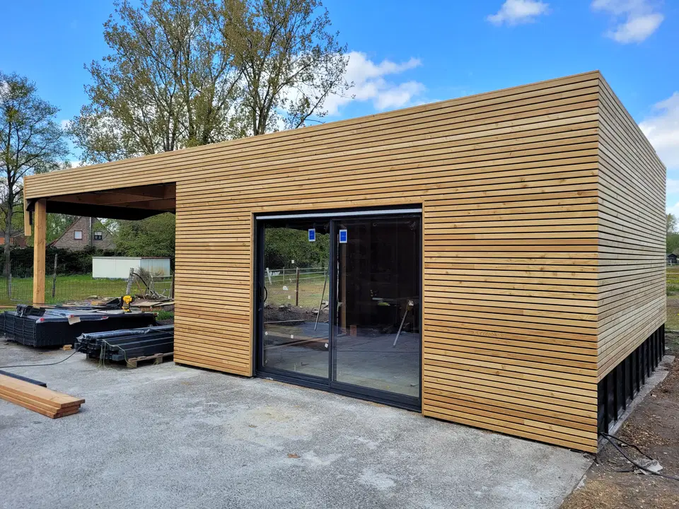 Le côté du pavillon : le carport prolonge la toiture, le soubassement noir court sous le bardage