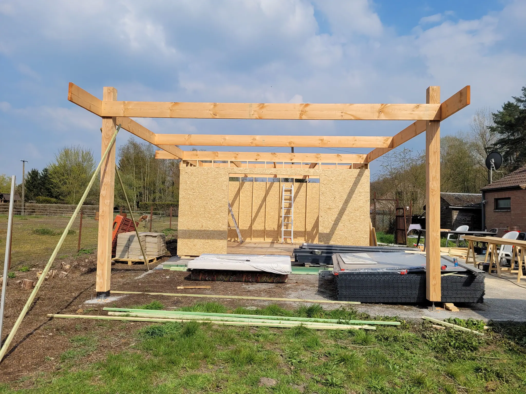 Le portique en bois massif levé sur la dalle, contreventé, devant le pré : il dessine déjà le volume et le carport
