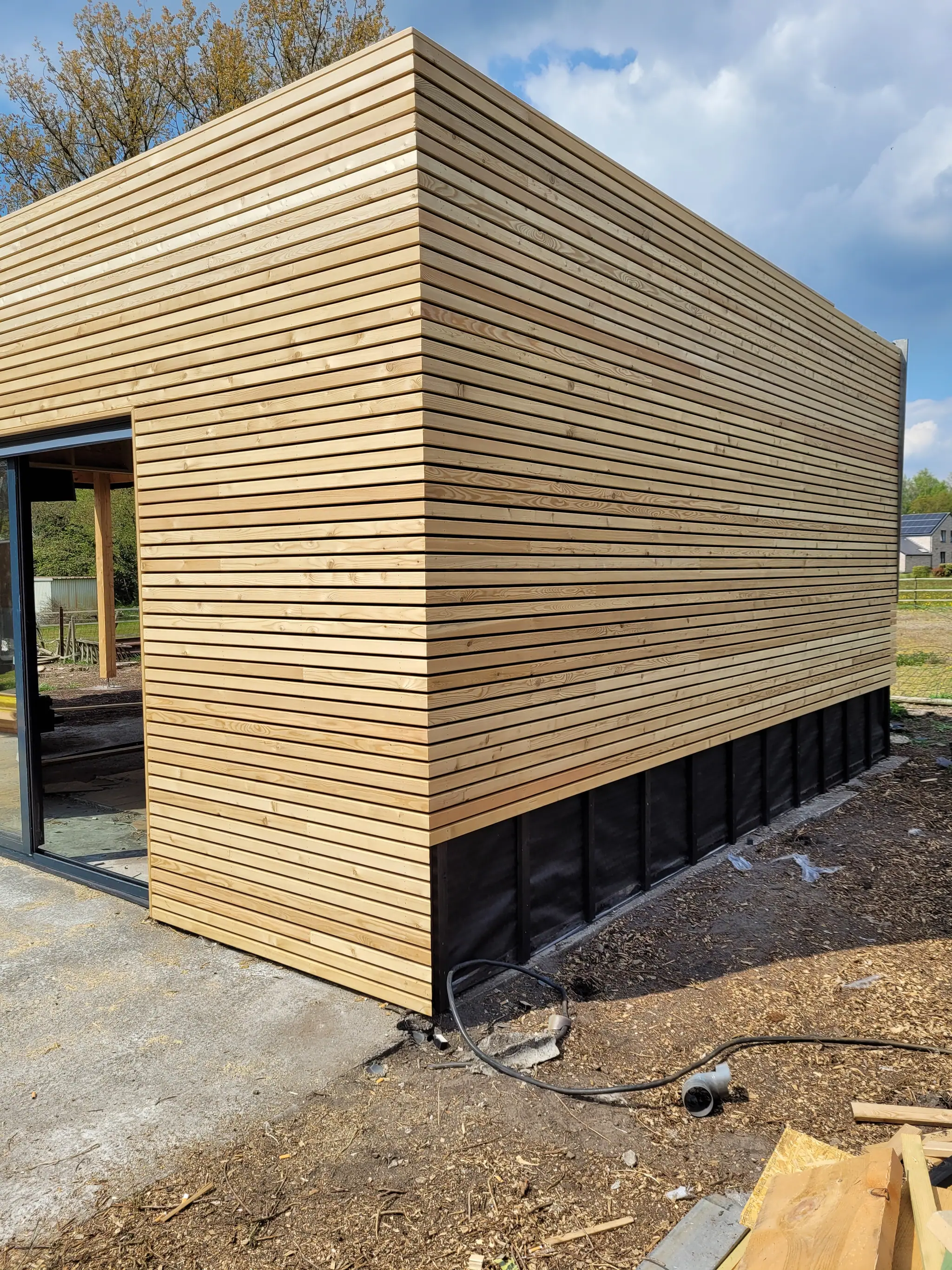 Le pavillon côté jardin, bardage et soubassement noir, la terre encore à niveler