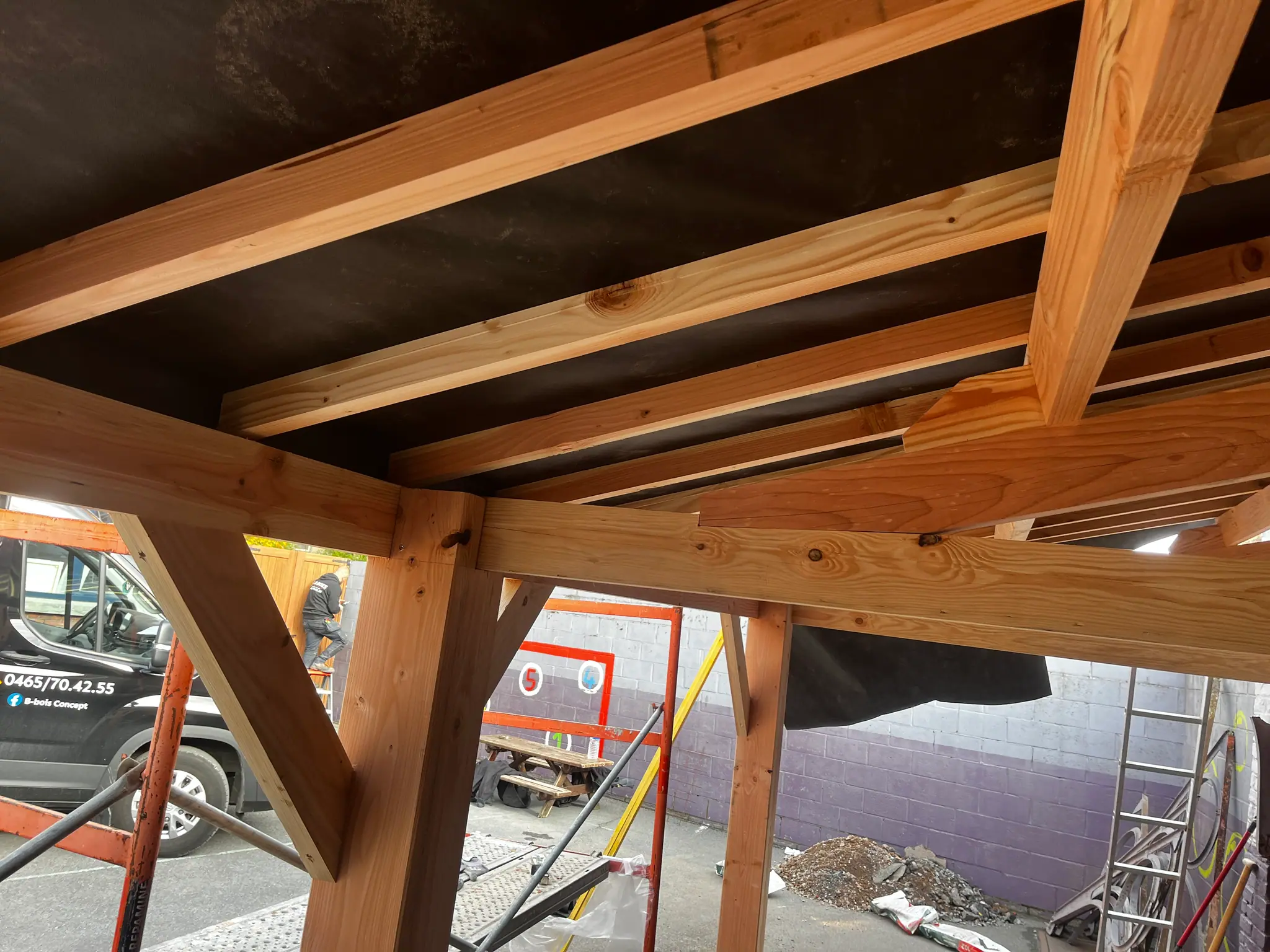 Vue en contre-plongée d’un préau en douglas massif : poteau, contrefiche et poutres, plancher au-dessus