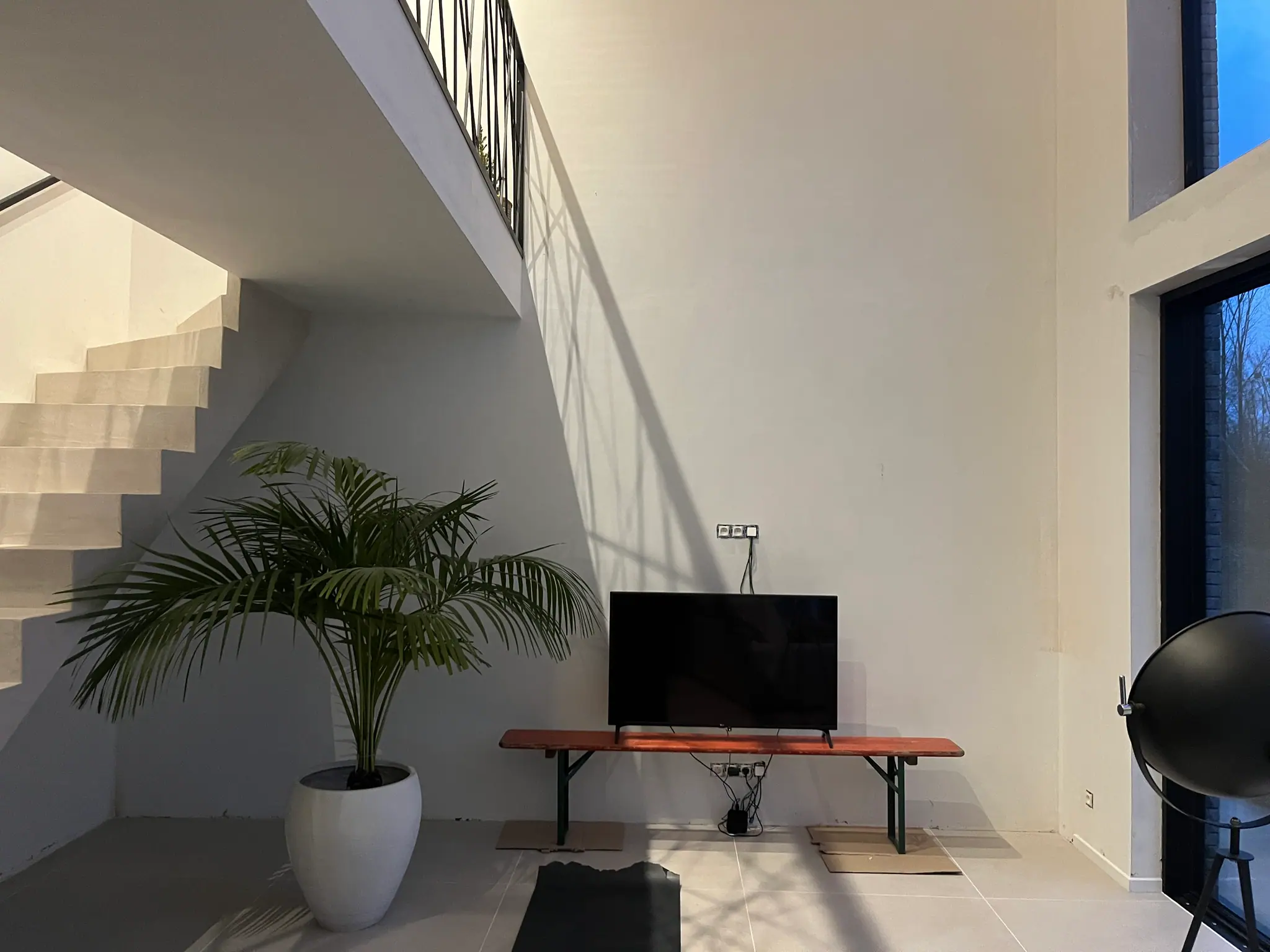 Le salon avant la pose : un mur blanc nu, un téléviseur sur un banc bas et l’escalier