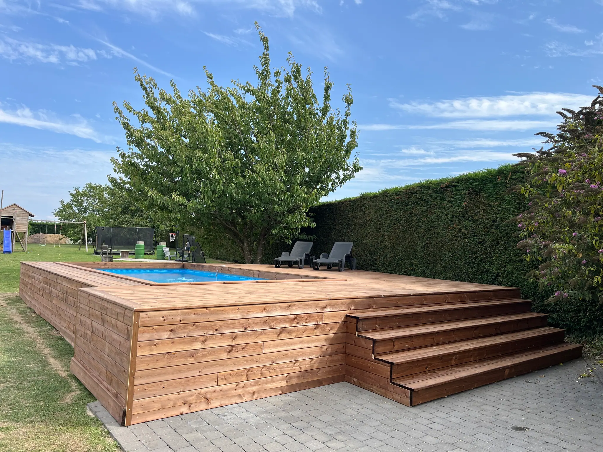 Platelage et large emmarchement autour d’une piscine, haie et arbuste fleuri