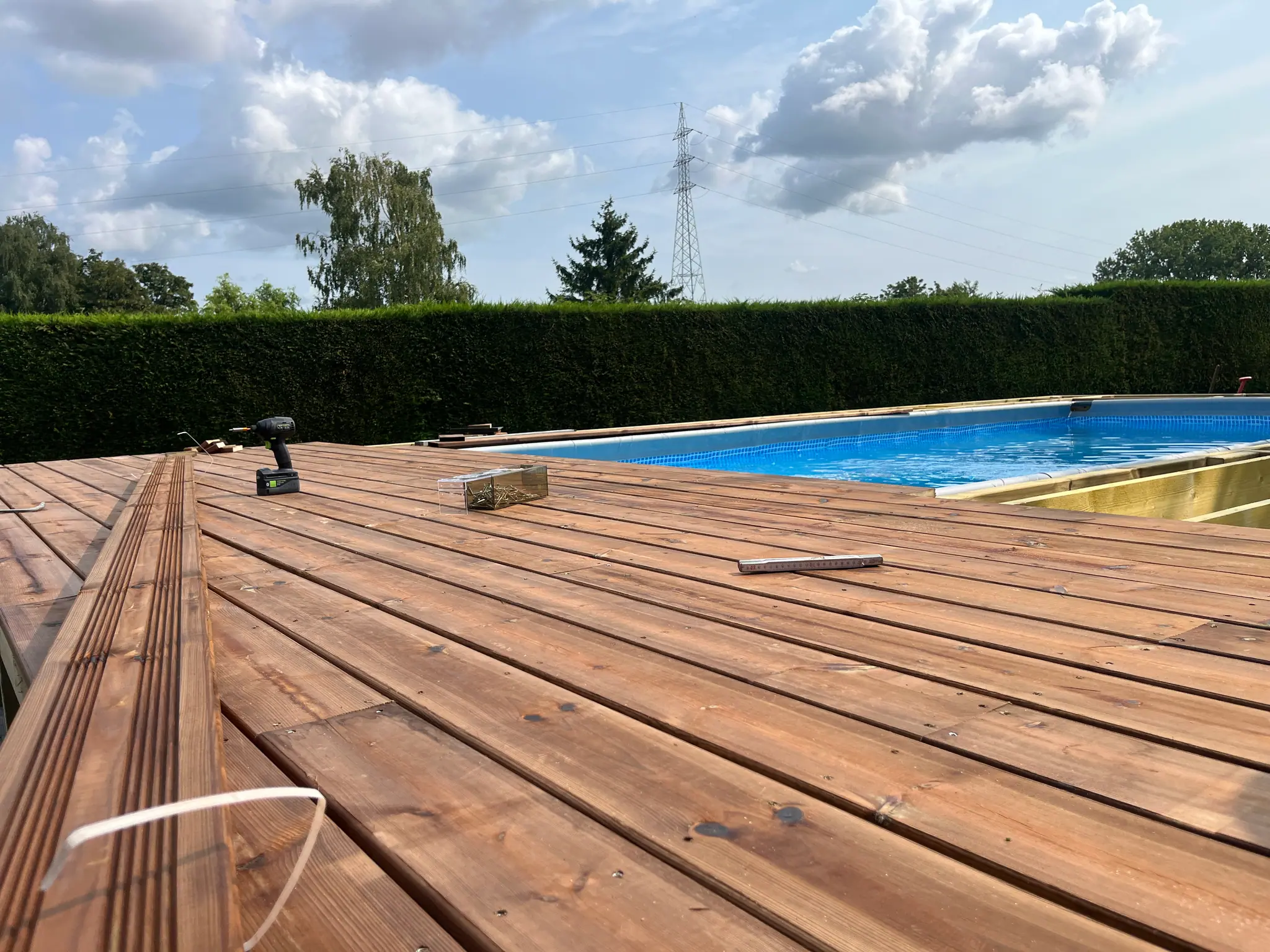 Les lames du platelage en cours de pose, visseuse posée dessus, les solives encore nues de l’autre côté du bassin